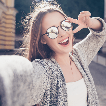 Woman posing with a bright white smile wearing sunglasses after her oral cancer screening.